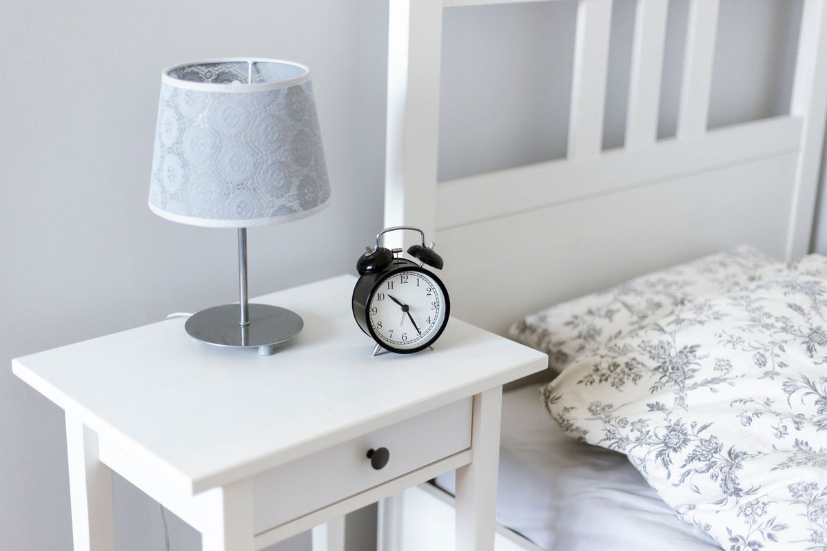 Analoge wekker en lamp op een wit nachtkastje naast het bed